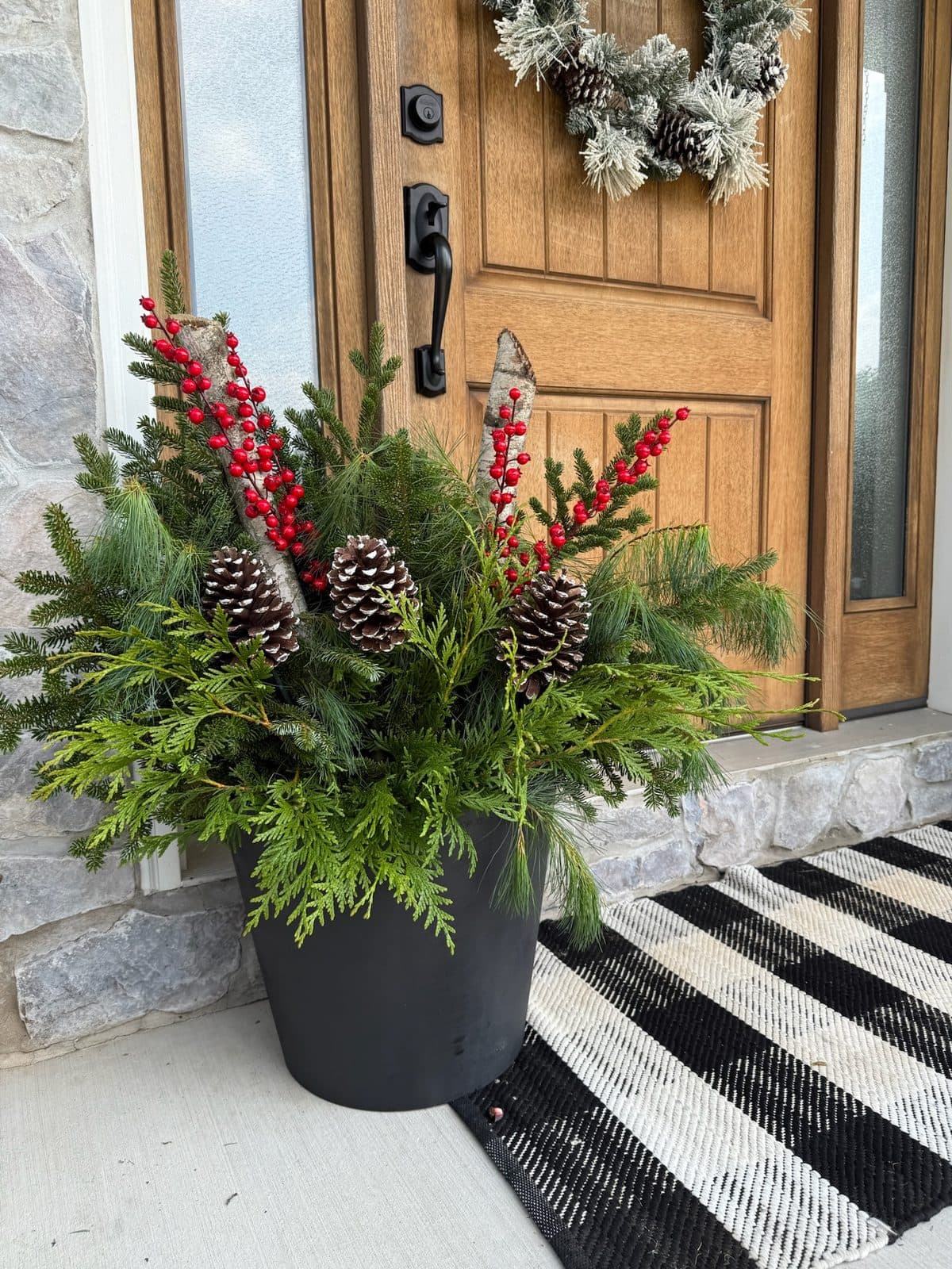 Winter greenery planter with pinecones, birch, and red berries by the front door